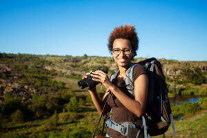beautiful african girl with backpack smiling, holding binoculars, canyon background.