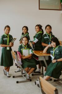 Group of Asian schoolgirls in green uniforms posing in classroom setting.