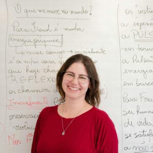 A cheerful female teacher standing in front of a whiteboard with handwriting.