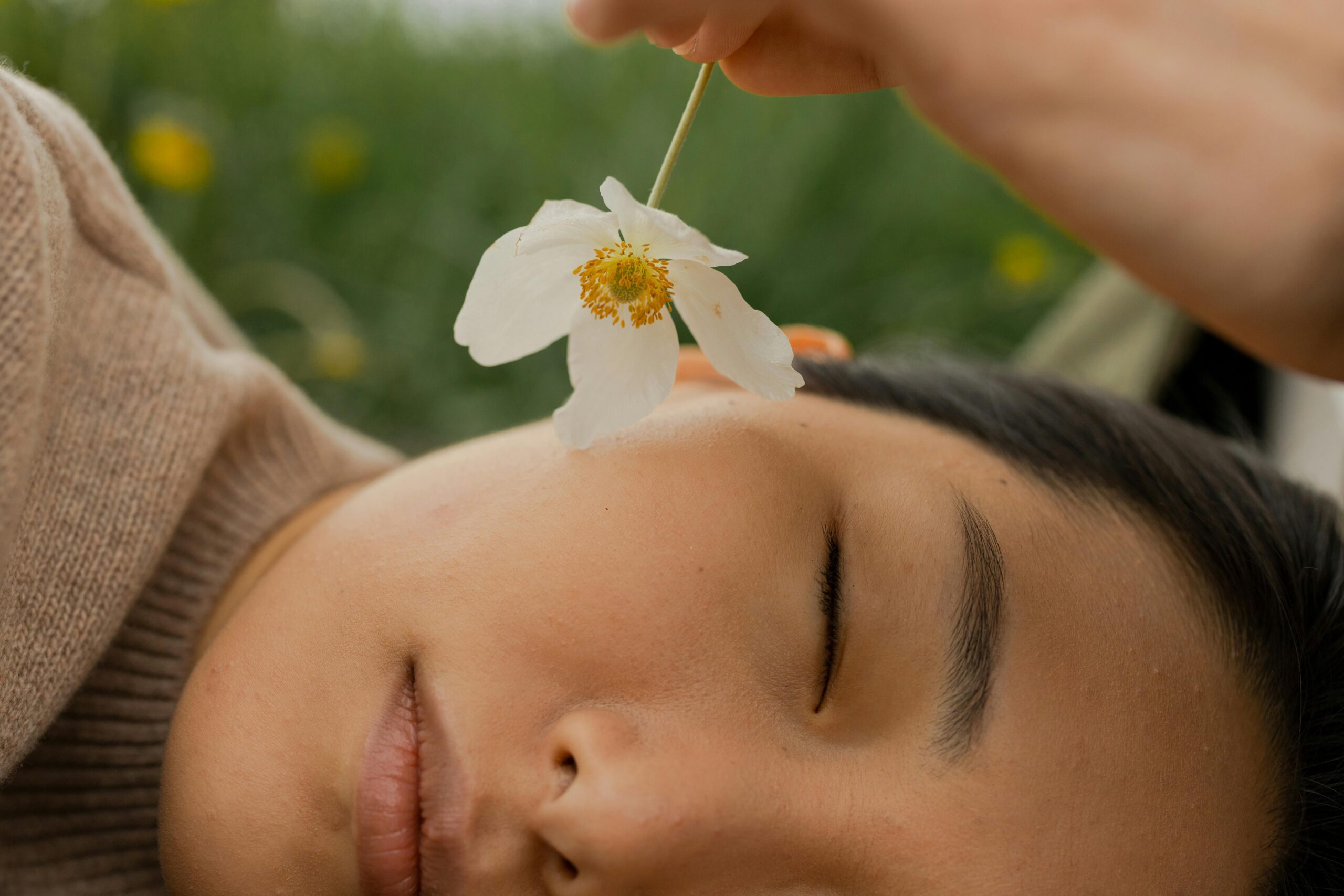 A serene moment outdoors with a playful touch of a flower on a woman's face.